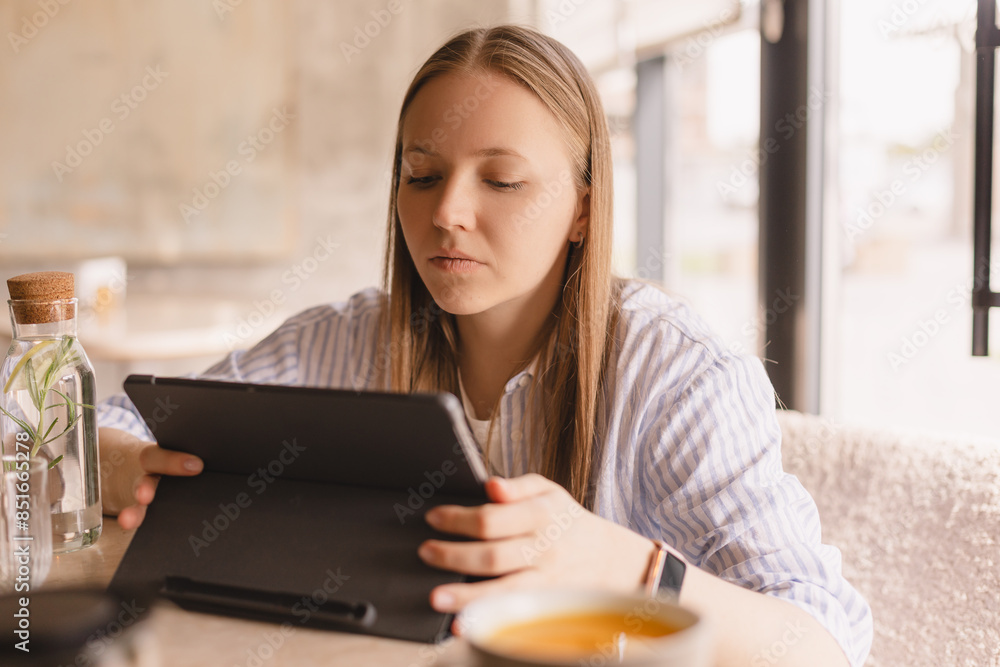 Attractive calm blonde woman wear shirt sitting with tablet computer in cafe. Beauty girl student using tablet computer for social media, studying or reading news. Attractive calm blonde woman wear shirt sitting with tablet computer in cafe. Beauty girl student using tablet computer for social media, studying or reading news.