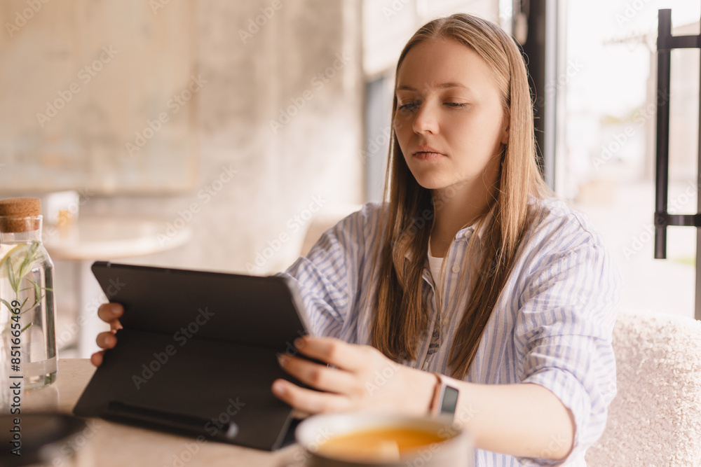 Attractive calm blonde woman wear shirt sitting with tablet computer in cafe. Beauty girl student using tablet computer for social media, studying or reading news. Attractive calm blonde woman wear shirt sitting with tablet computer in cafe. Beauty girl student using tablet computer for social media, studying or reading news.