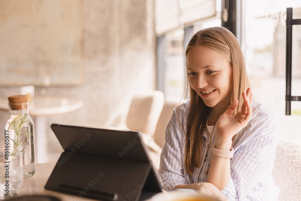 Blonde happy young woman with tablet pc computer having video conference at restaurant, girl waving her hand, say hi hello, streamer.