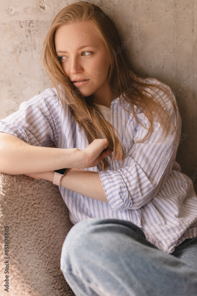 Portrait of blonde woman posing for portrait at home, sitting on comfortable armchair, looking with smile, laughing, fix her hair. Girl look sensual and dreaming wear shirt and jeans look side. Portrait of blonde woman posing for portrait at home, sitting on comfortable armchair, looking with smile, laughing, fix her hair. Girl look sensual and dreaming wear shirt and jeans look side.