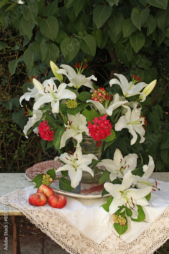 Still life of white lilies and red hydrangeas in a vase on a a table with white lace cloth