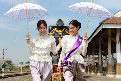 Traveler Asia Two sisters wear Thai traditional dress with an umbrella while walking on the railway train platform, in Bangkok, Thailand