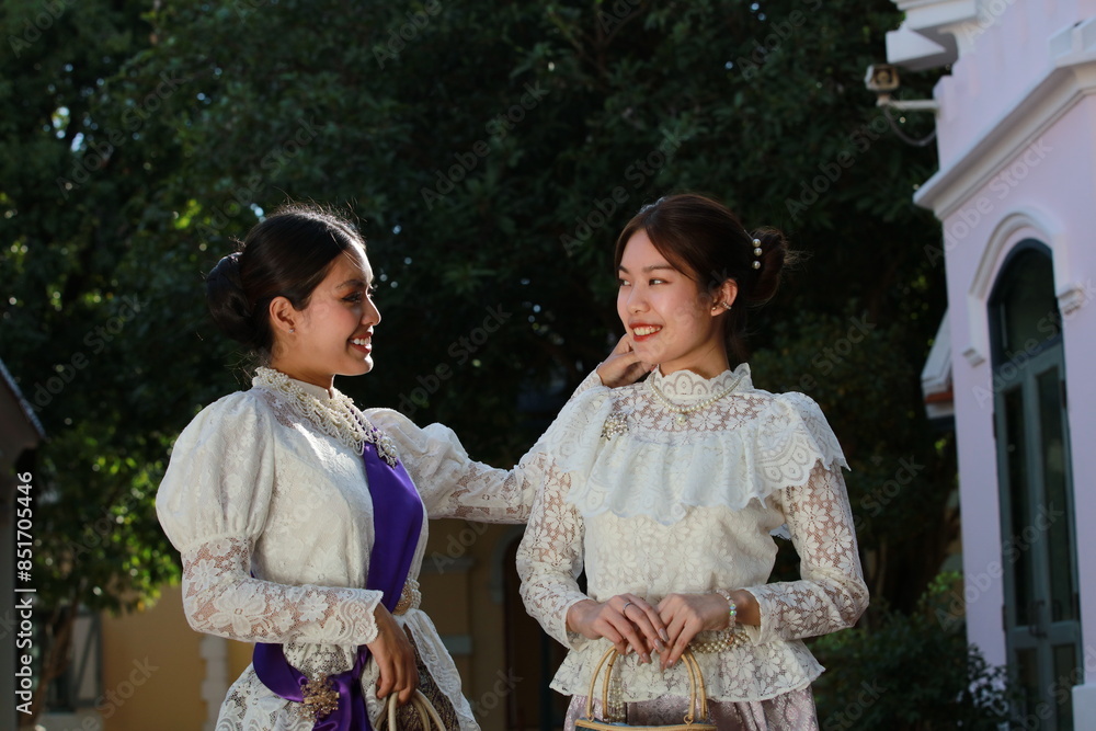 Portrait of two Asian women in Thai traditional dress standing together on the way to an ancient train station with beautiful art and architecture, they also smile and look at the camera. Portrait of two Asian women in Thai traditional dress standing together on the way to an ancient train station with beautiful art and architecture, they also smile and look at the camera.