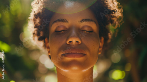 Close-up of a womanâs face, deeply relaxed in a group meditation in a tranquil forest, with sunlight highlighting her peaceful expression.