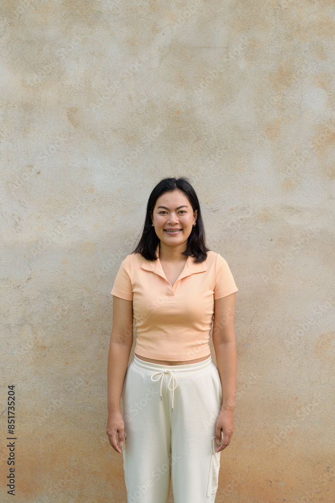 Asian woman against a wall background wearing a light peach polo shirt and white pants Asian woman against a wall background wearing a light peach polo shirt and white pants