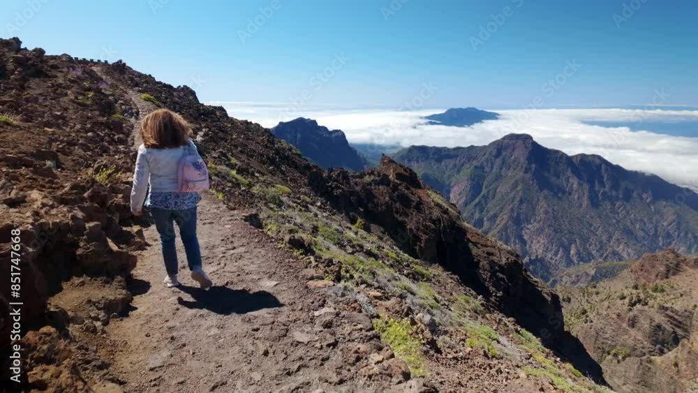 Woman hiker walking along a path between volcanic rocks at the top of the mountain, La Palma. Woman hiker walking along a path between volcanic rocks at the top of the mountain, La Palma.