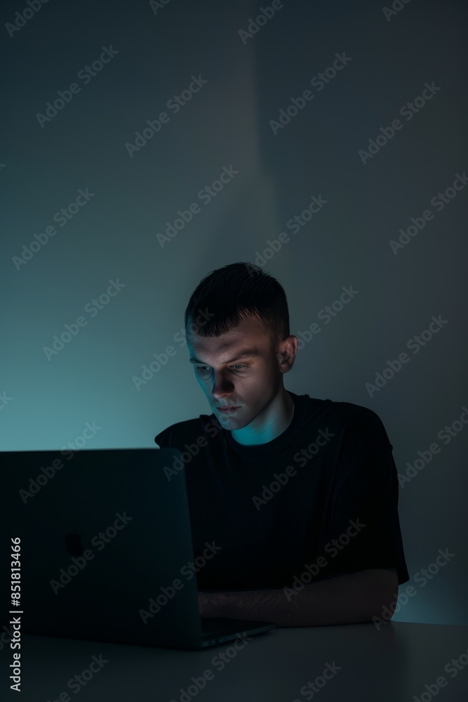 Young man focused on work or study on his laptop in a dark room, illuminated by the screen's light. Young man focused on work or study on his laptop in a dark room, illuminated by the screen's light.
