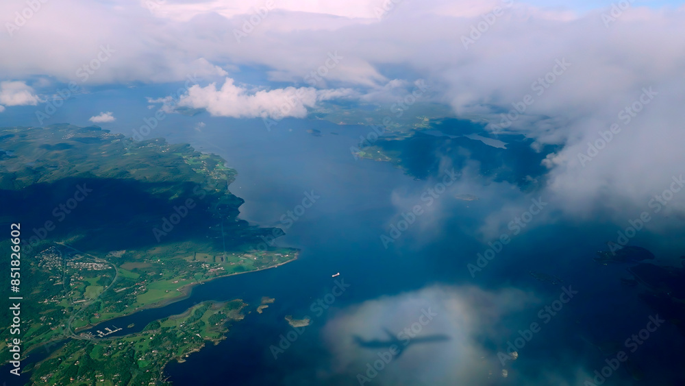 Aerial view through the clouds to the Norwegian fjords, shadow of an airplane on a cloud. Top view from the clouds to the sea bay with coastal hills Aerial view through the clouds to the Norwegian fjords, shadow of an airplane on a cloud. Top view from the clouds to the sea bay with coastal hills