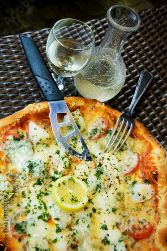 Delicious seafood pizza with scallops on wicker brown table in rustic pizzeria restaurant served with cold white house wine in pitcher. photo