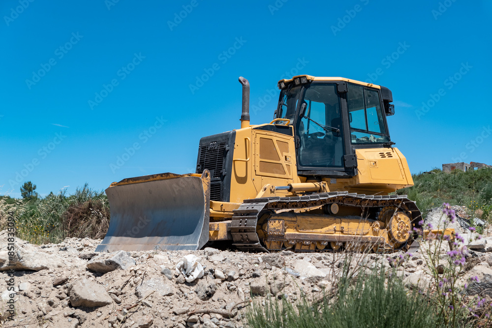Bulldozer de esteiras a operar num terreno rochoso sob um céu azul Bulldozer de esteiras a operar num terreno rochoso sob um céu azul