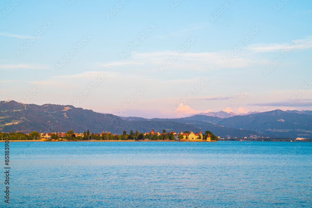 Germany, Warm orange sunset light shining on alps behind water of bodensee in summer with snow covered peaks next to old town of lindau city Germany, Warm orange sunset light shining on alps behind water of bodensee in summer with snow covered peaks next to old town of lindau city