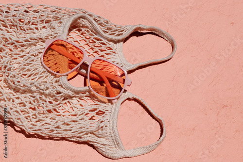 Mesh tote with orange-colored sunglasses on a coral textured background