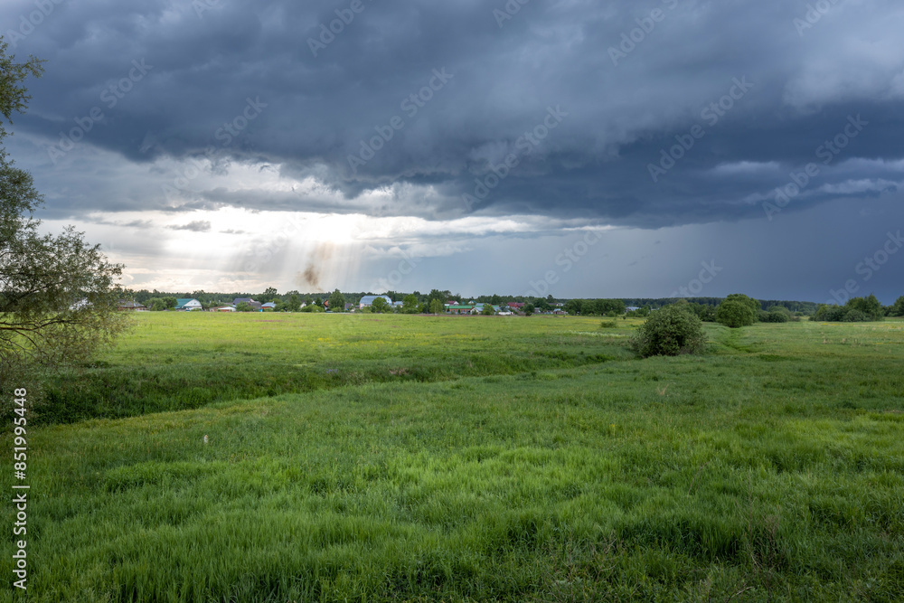 A wide shot of a green field in the countryside, with a dramatic stormy sky above. The sun breaks through the clouds, casting a spotlight on the landscape. A wide shot of a green field in the countryside, with a dramatic stormy sky above. The sun breaks through the clouds, casting a spotlight on the landscape.