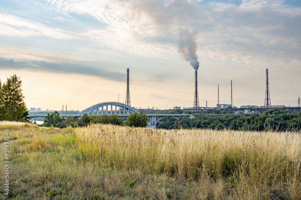 A bridge spans a river with a large industrial plant in the background A bridge spans a river with a large industrial plant in the background