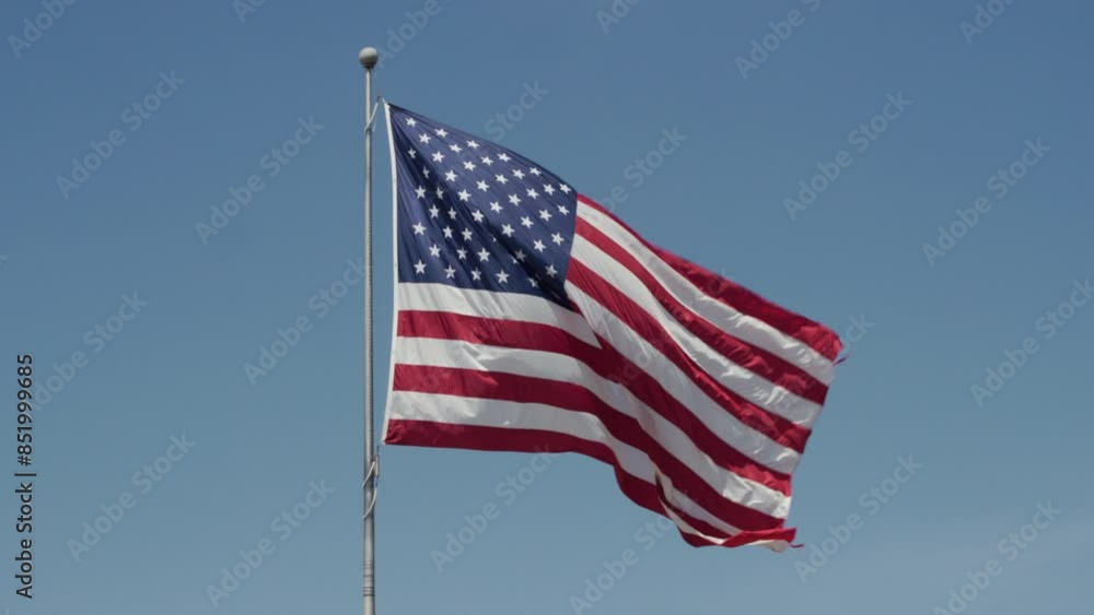 American Flag Waving on Pole in The Wind Against Blue Sky American Flag Waving on Pole in The Wind Against Blue Sky