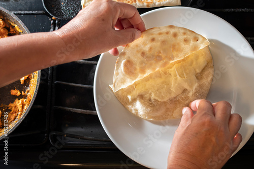 Concept of taking or grabbing food with hands, feminine Mexican hands prepring a flour tortilla and cheese to make a quesadilla on a white plate. photo