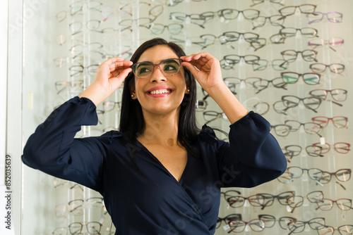 Fényképezés Hispanic Woman trying on different eyeglass frames and smiling at the optometris
