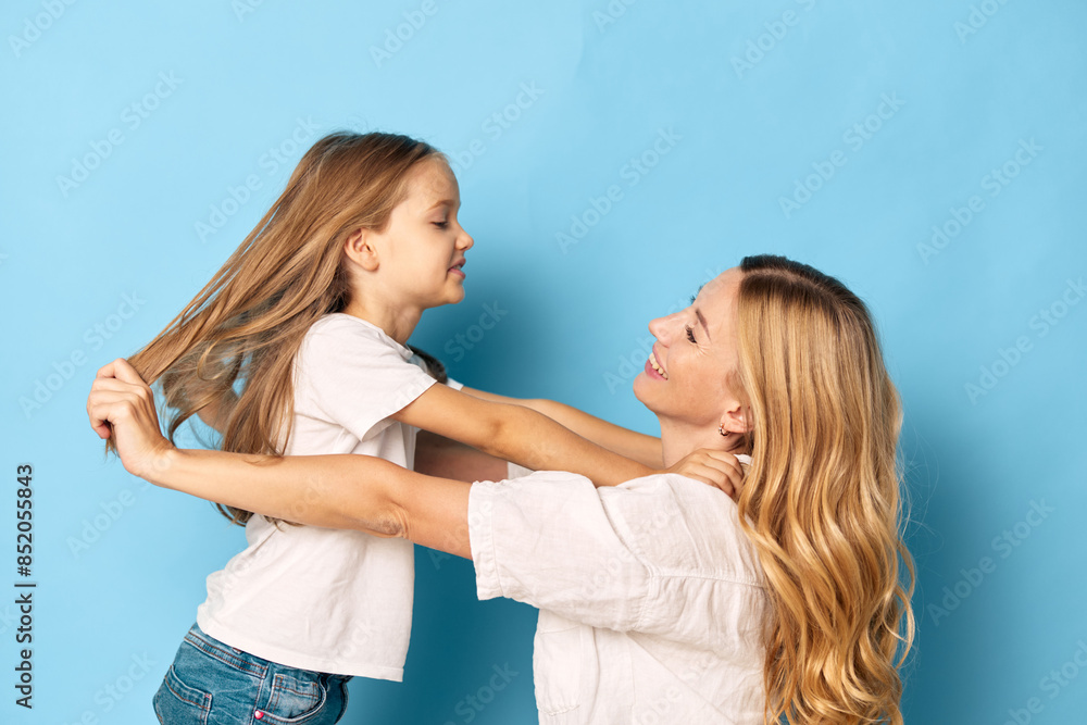 Joyful mother and daughter playing together against a vibrant blue background, capturing a moment of playful bonding and happiness Joyful mother and daughter playing together against a vibrant blue background, capturing a moment of playful bonding and happiness