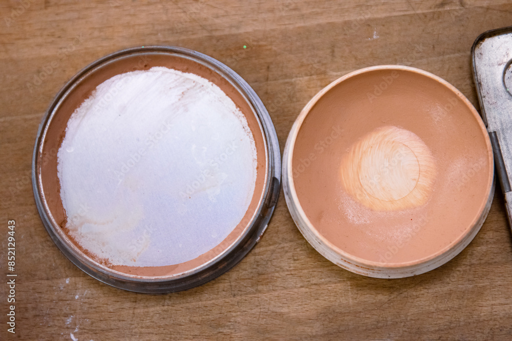 Used half empty makeup powder on the wooden table. Skin tone, pink color. Bronzer or highlighter in brown beige. Eyeshadow palette. Old and dirty sponge. Close up. Copy space. Selective focus. Used half empty makeup powder on the wooden table. Skin tone, pink color. Bronzer or highlighter in brown beige. Eyeshadow palette. Old and dirty sponge. Close up. Copy space. Selective focus.
