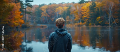Back view of a man wearing sweatshirt standing in front of lake with forest blurred background AI generated © dheograft