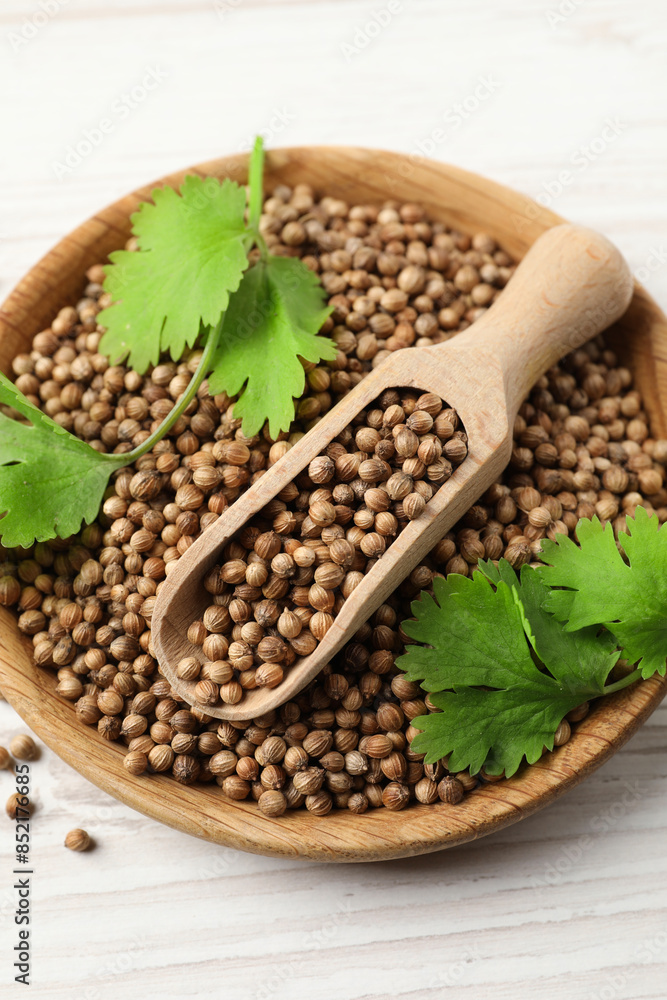 Dried coriander seeds with green leaves in bowl and scoop on wooden table, top view Dried coriander seeds with green leaves in bowl and scoop on wooden table, top view