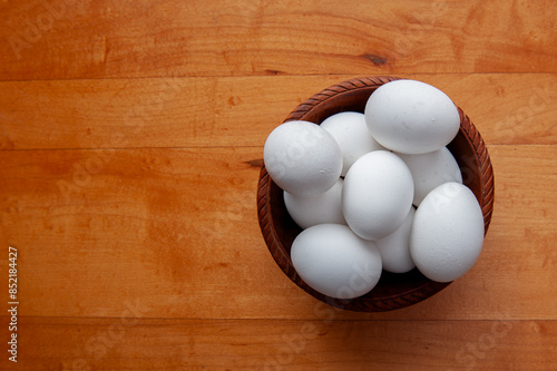 Plain white eggs in a wooden bowl on a wood table