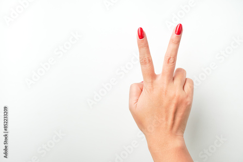 A woman's hand with bright red nail polish is making a raising peace hand gesture. Isolated on white background - Cut Out