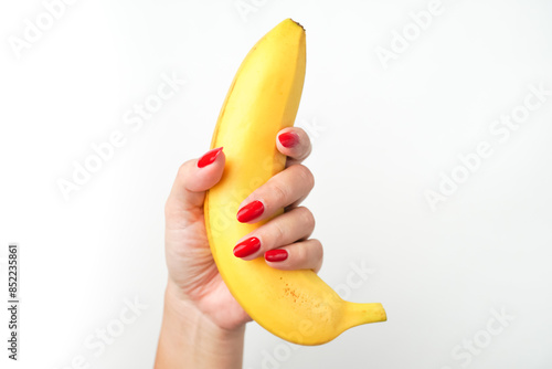 Hands of a woman with bright red nail polish holding large curvy banana fruit isolated on white background. Illustration for sex workers, sexual scenes, and male genitalia penis.