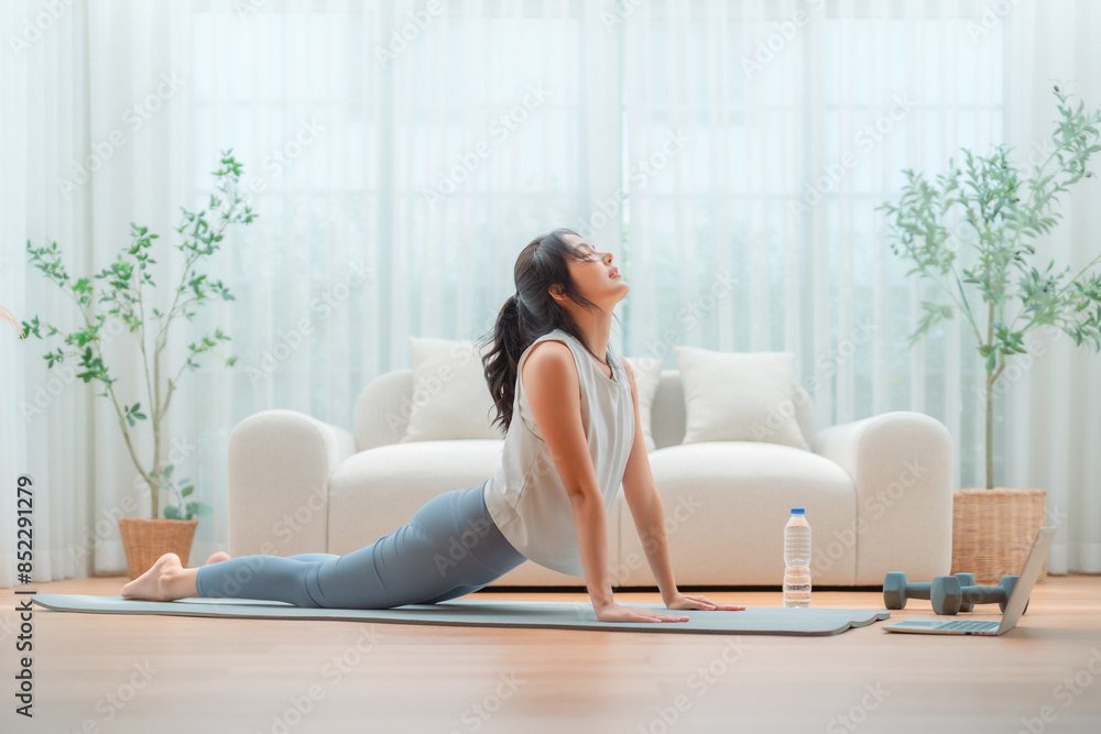 Young Asian woman stretching yoga workout on exercise mat while online training class with computer laptop in living room Young Asian woman stretching yoga workout on exercise mat while online training class with computer laptop in living room
