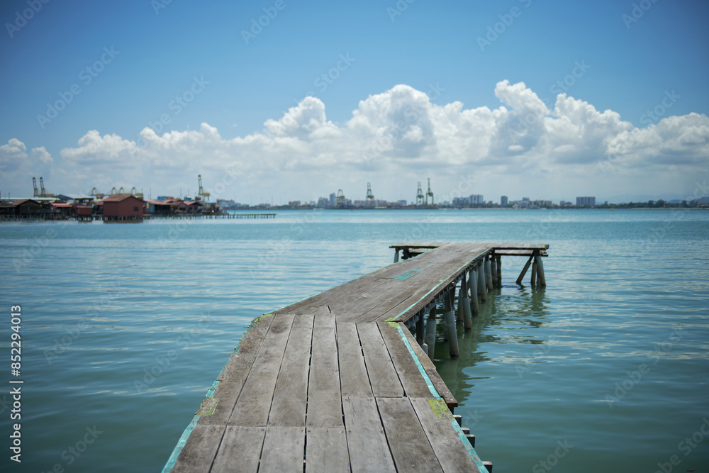 Fototapeta premium A vintage wooden bridge extends into the sea against blue sky background. Selective focus.