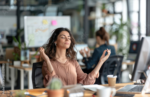 A woman meditating at her desk in an office, using the Zen Wadang to keep calm and focused during work with a meditation app on her computer screen. photo