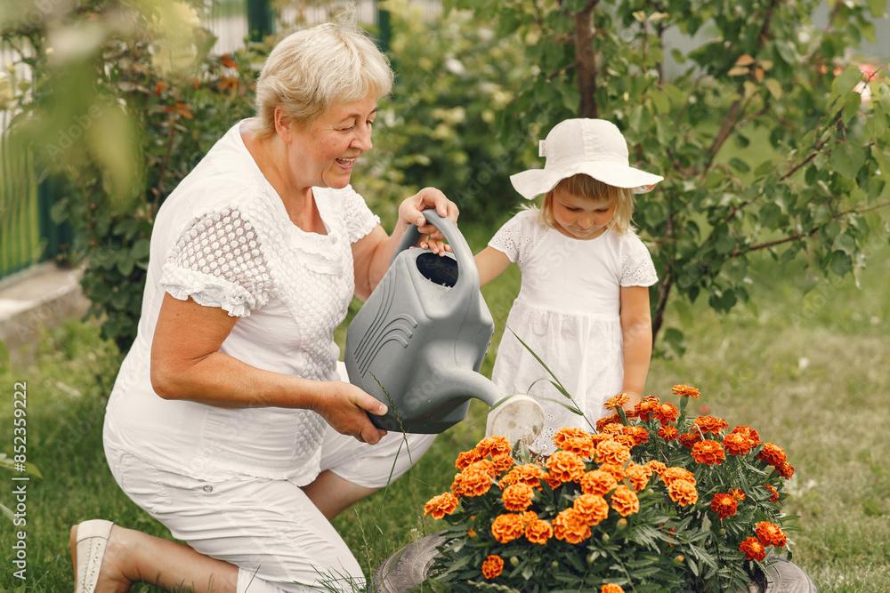 Little girl and her grandmother watering flowers in garden Little girl and her grandmother watering flowers in garden
