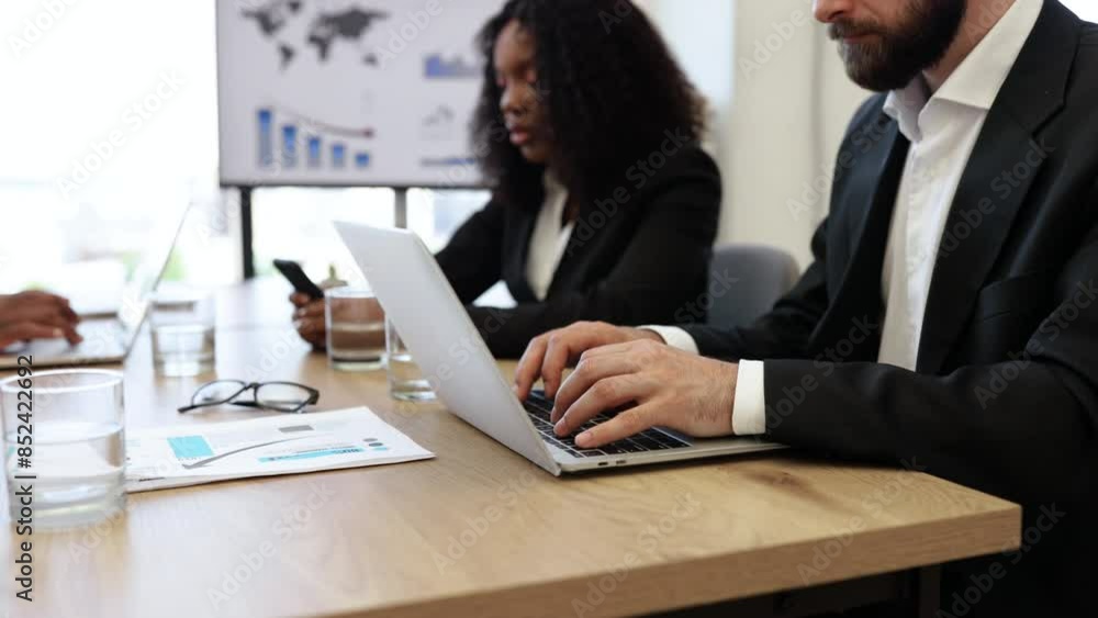 Colleagues engaged in a business meeting, working on laptops and discussing charts and graphs. The office setting and professional attire indicate a formal and productive work environment. Colleagues engaged in a business meeting, working on laptops and discussing charts and graphs. The office setting and professional attire indicate a formal and productive work environment.