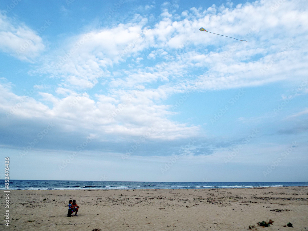 A father and son fly a kite on a wild and deserted beach. Blue sky with clouds. A father and son fly a kite on a wild and deserted beach. Blue sky with clouds.