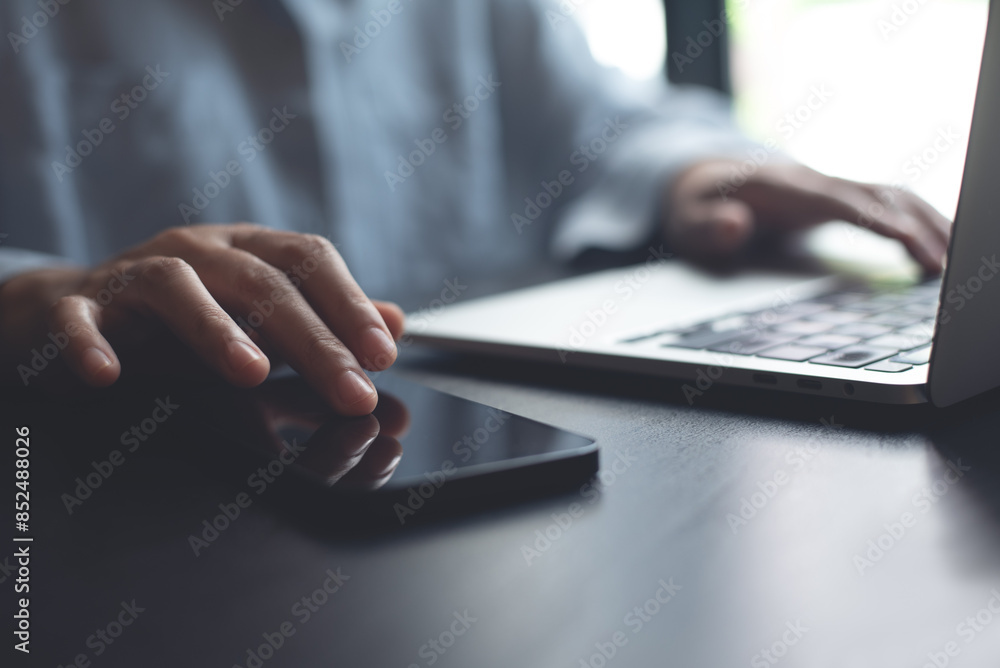 Woman using smartphone while sitting at table working on laptop computer at home office, online shopping Woman using smartphone while sitting at table working on laptop computer at home office, online shopping
