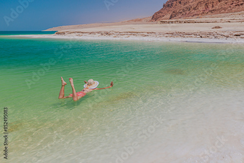 Woman making thalassotherapy enjoys a peaceful float in clear green waters of Dead Sea, showcasing a relaxed beach lifestyle and the joy of summer vacations in Jordan