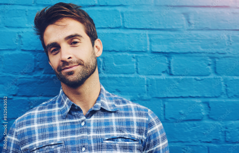 Man, wall and portrait with smile in city with fashion, confidence and outdoor with trendy style. Person, cool and edgy clothes for streetwear by urban building, sidewalk and blue shirt in metro