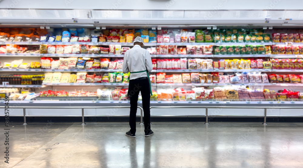 Fototapeta premium Worker male employee in an apron stands on supermarket dairy product section