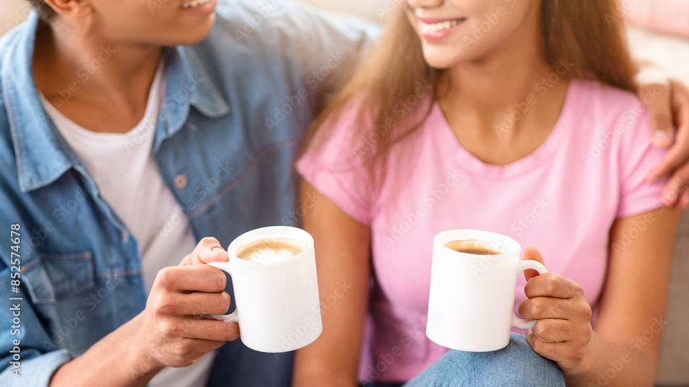 This image shows a teen couple enjoying a cup of coffee together while sitting indoors. They are both smiling and seem to be enjoying each others company, cropped This image shows a teen couple enjoying a cup of coffee together while sitting indoors. They are both smiling and seem to be enjoying each others company, cropped