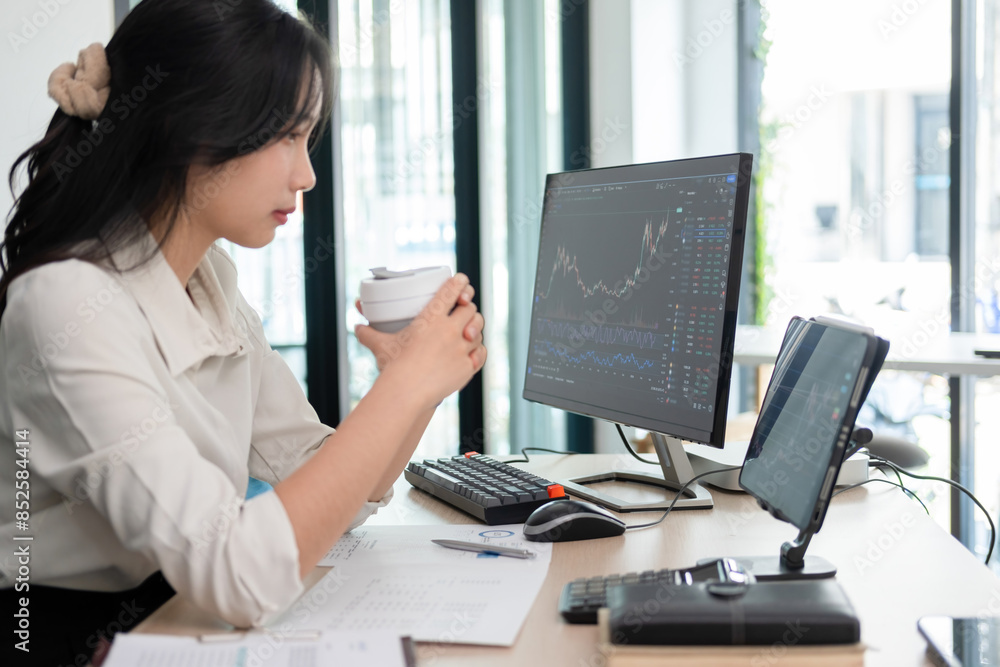 Woman examines stock graphs while enjoying coffee Woman examines stock graphs while enjoying coffee