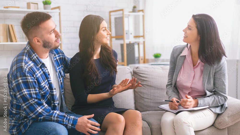 A couple sits on a couch in a therapists office while the therapist listens intently to the woman concerns. The man sits next to her, providing support and listening to their conversation. A couple sits on a couch in a therapists office while the therapist listens intently to the woman concerns. The man sits next to her, providing support and listening to their conversation.
