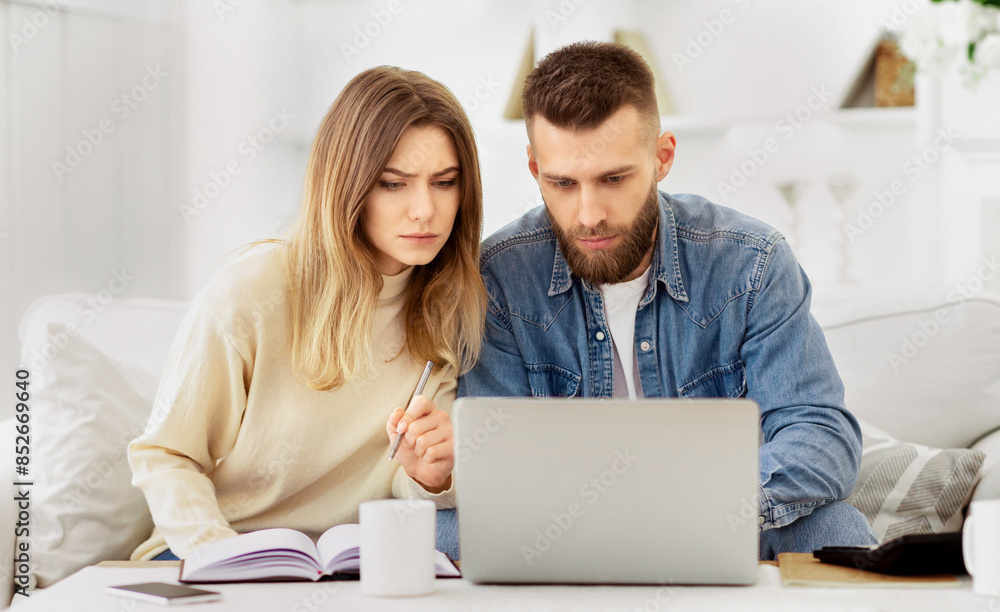 A man and a woman seated, focusing on a laptop screen in front of them. A man and a woman seated, focusing on a laptop screen in front of them.