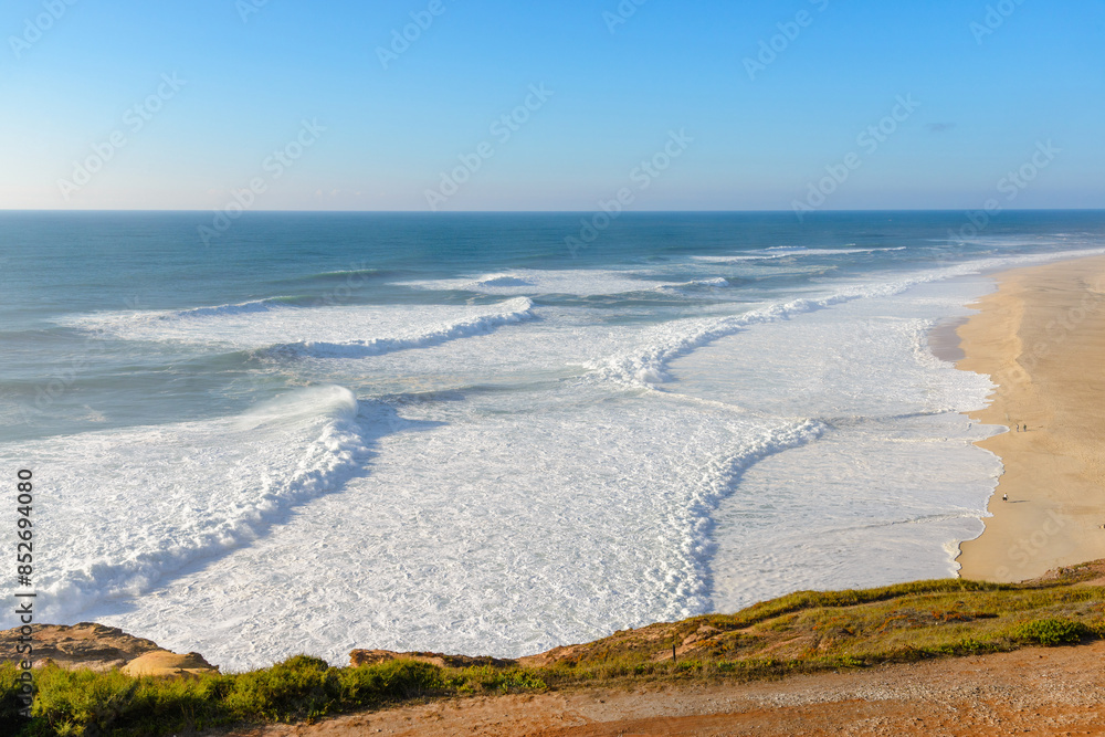 Fototapeta premium Aerial view of sandy beach and Atlantic ocean with big waves in Nazare, Portugal. Surfing paradise town in Portugal, Europe