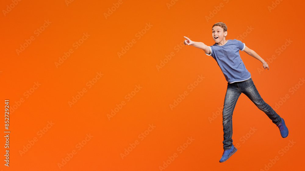 Wow, look! Excited amazed boy jumping and pointing hand to empty space aside, orange studio background Wow, look! Excited amazed boy jumping and pointing hand to empty space aside, orange studio background