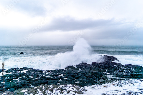 Cliffs in Valahnúkamöl in Iceland in winter time covered with snow, stormy sea, high waves and black rocks