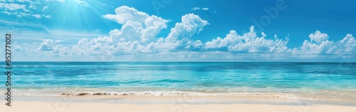 A panoramic view of a calm ocean with a sandy beach in the foreground. The clear blue sky is dotted with fluffy white clouds and the sun is shining brightly. The water is a vibrant turquoise color, cr