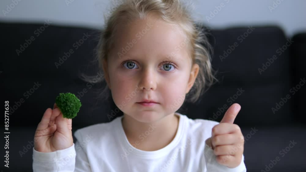 Caucasian girl holds broccoli eats it looking at camera healthy eating vegetables close up to face. With broccoli in hands little girl looks at camera eating vegetables nutritious foods vegetables. Caucasian girl holds broccoli eats it looking at camera healthy eating vegetables close up to face. With broccoli in hands little girl looks at camera eating vegetables nutritious foods vegetables.