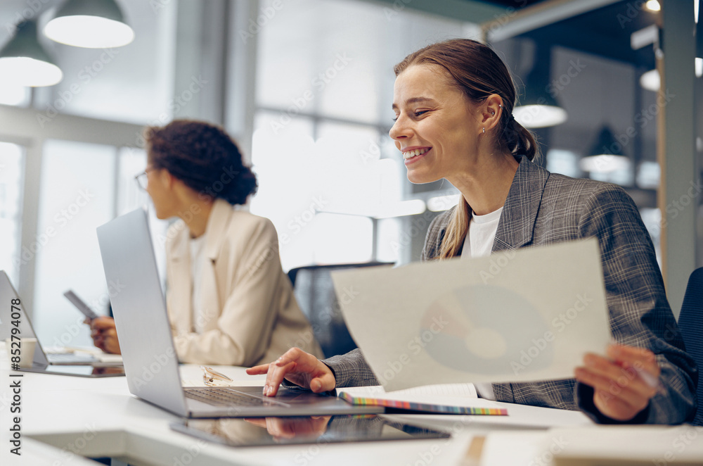 Smiling female accountant working with financial statement and use laptop while sitting in office Smiling female accountant working with financial statement and use laptop while sitting in office