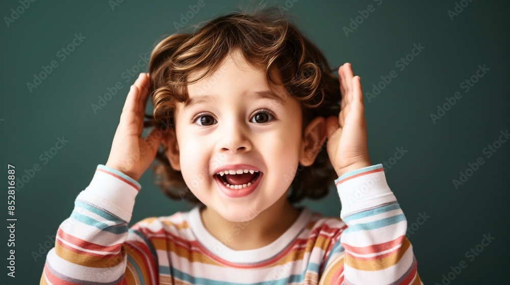 Joyful young child with curly hair wearing a striped shirt, hands raised near their head, smiling exuberantly while looking directly at the camera. Joyful young child with curly hair wearing a striped shirt, hands raised near their head, smiling exuberantly while looking directly at the camera.