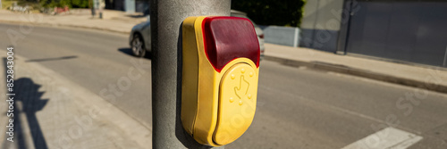 Accessible pedestrian crossing button on an urban pole with a tactile and visual signal for safe street crossing, related to disability awareness and urban design